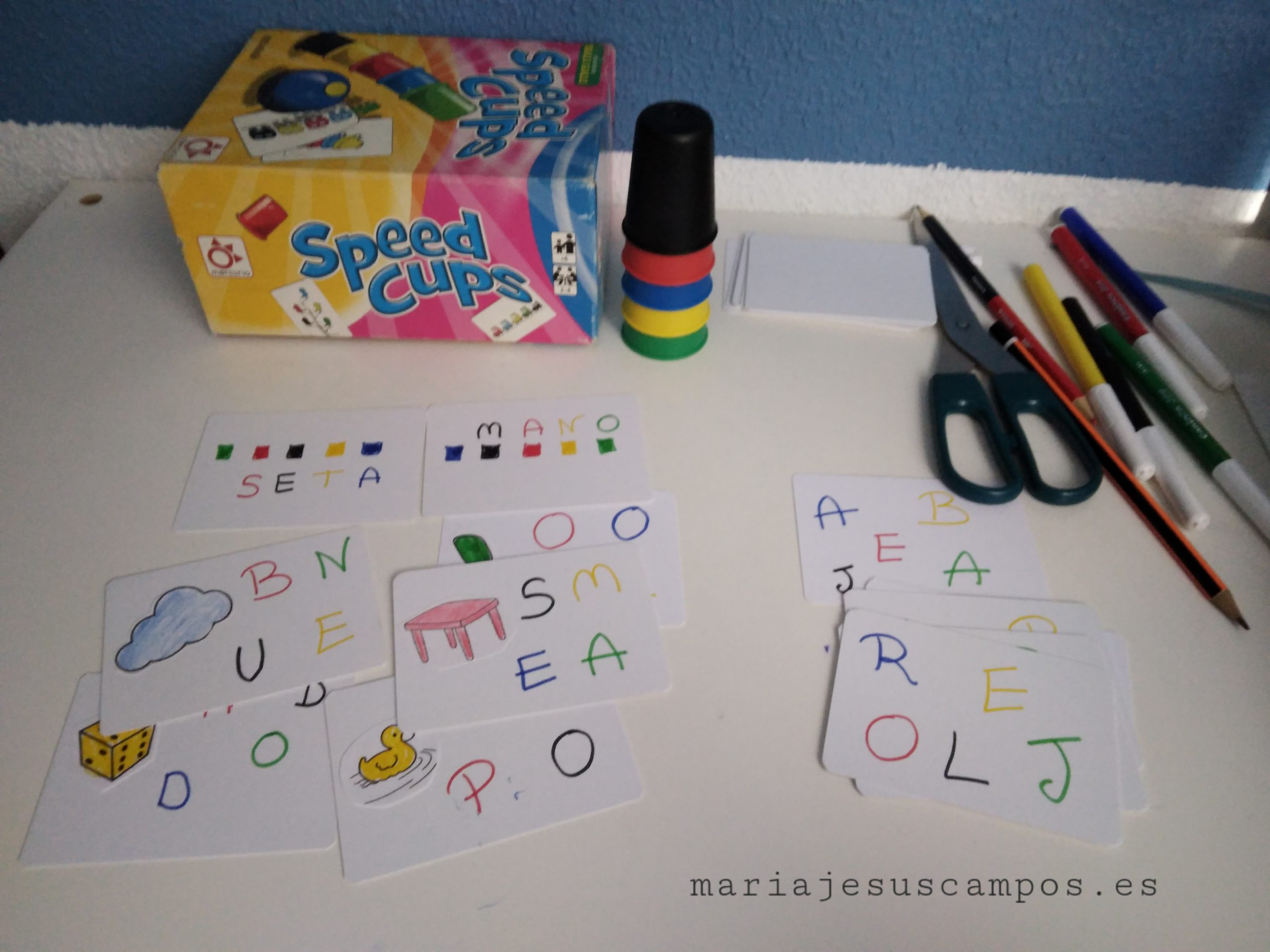 El juego speed cups con tarjetas hechas a mano en las que aparecen palabras con letras de color negro, rojo, amarillo, verde y azul.